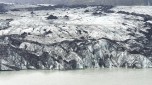 Eine Gletscherzunge die in Wasser endet. Das Eis ist schwarz wei durch Vulkanasche gefrbt